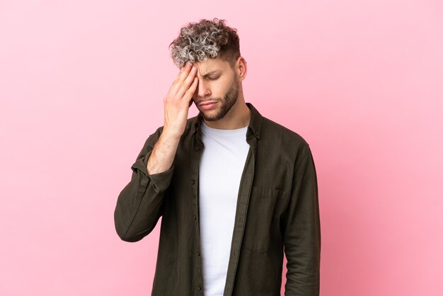 Young handsome caucasian man isolated on pink background with headache