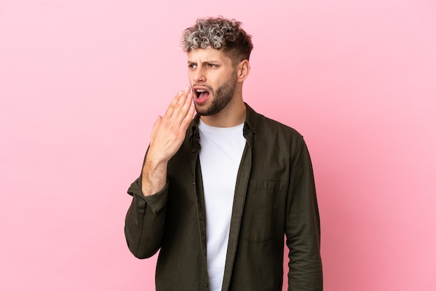 Young handsome caucasian man isolated on pink background yawning and covering wide open mouth with hand