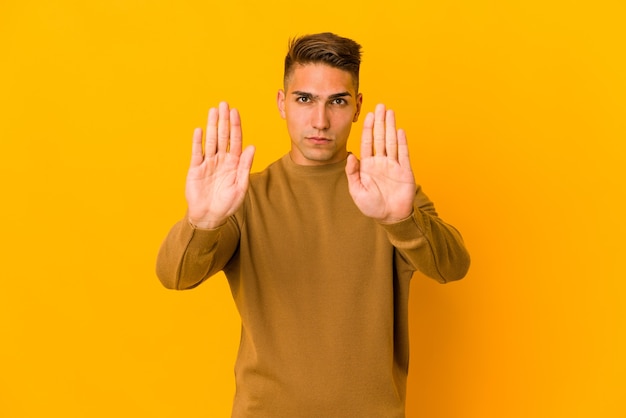 Young handsome caucasian man isolated standing with outstretched hand showing stop sign, preventing you.