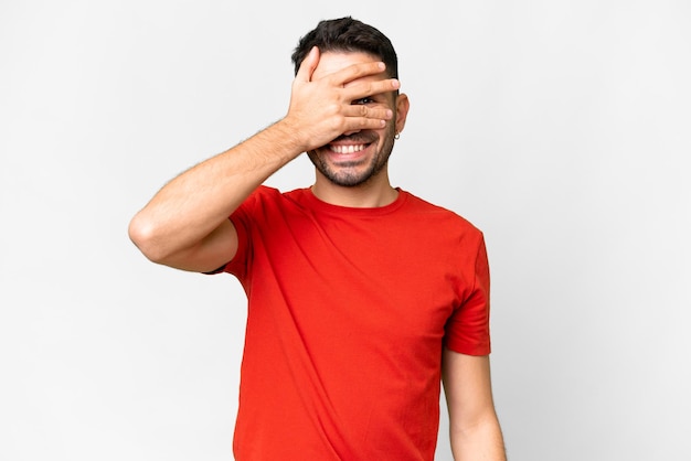 Young handsome caucasian man over isolated white background covering eyes by hands and smiling