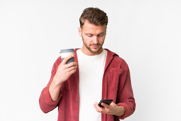 コーヒーと携帯電話を手に取るために,孤立した白い背景の上に若いハンサムな白人男性