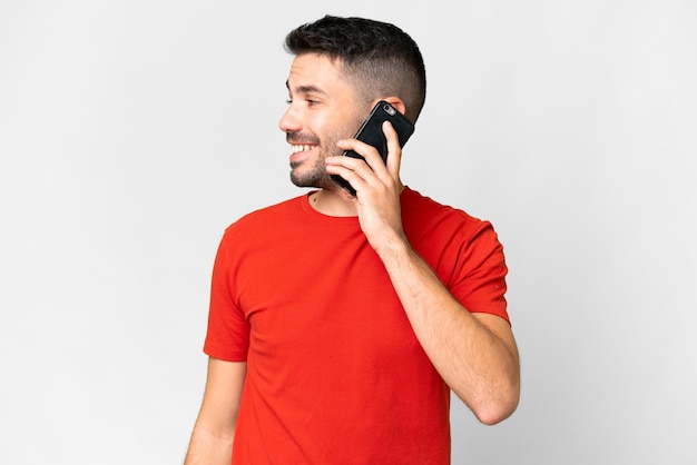 Young handsome caucasian man over isolated white background keeping a conversation with the mobile phone with someone