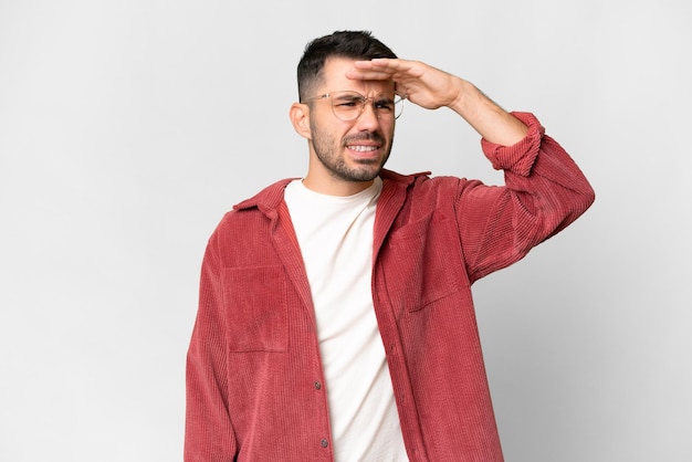 Young handsome caucasian man over isolated white background looking far away with hand to look something