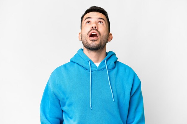 Young handsome caucasian man over isolated white background looking up and with surprised expression