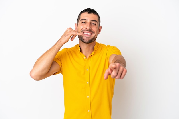 Young handsome caucasian man isolated on white background making phone gesture and pointing front