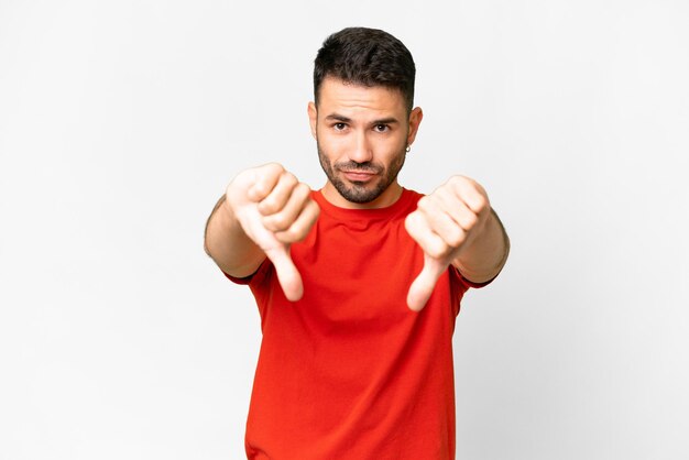 Young handsome caucasian man over isolated white background showing thumb down with two hands