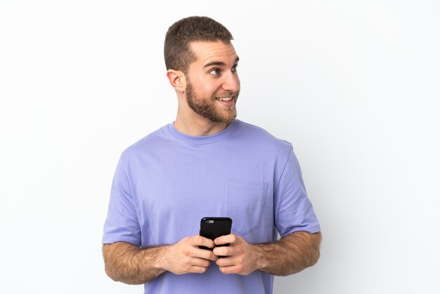 Young handsome caucasian man isolated on white background using mobile phone and looking up