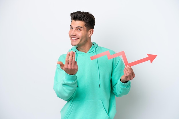 Photo young handsome caucasian man isolated on white bakcground holding a catching a rising arrow and doing coming gesture