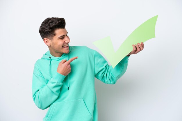 Young handsome caucasian man isolated on white bakcground holding a check icon and pointing it