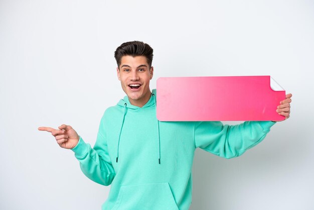 Young handsome caucasian man isolated on white bakcground holding an empty placard and pointing side