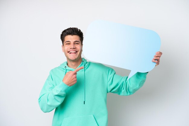 Young handsome caucasian man isolated on white bakcground holding an empty speech bubble and pointing it