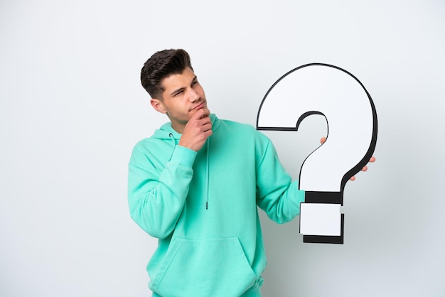 Young handsome caucasian man isolated on white bakcground holding a question mark icon and having doubts