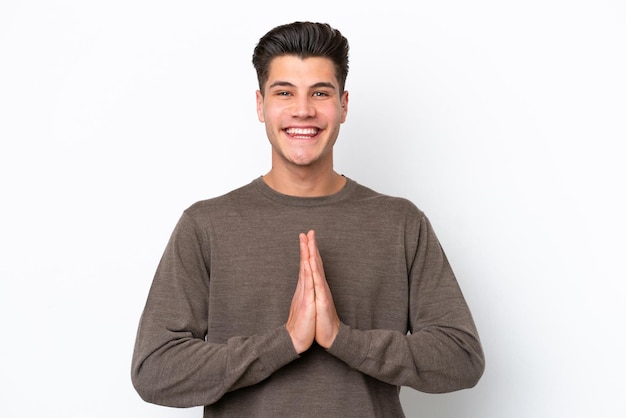 Young handsome caucasian man isolated on white bakcground keeps palm together Person asks for something