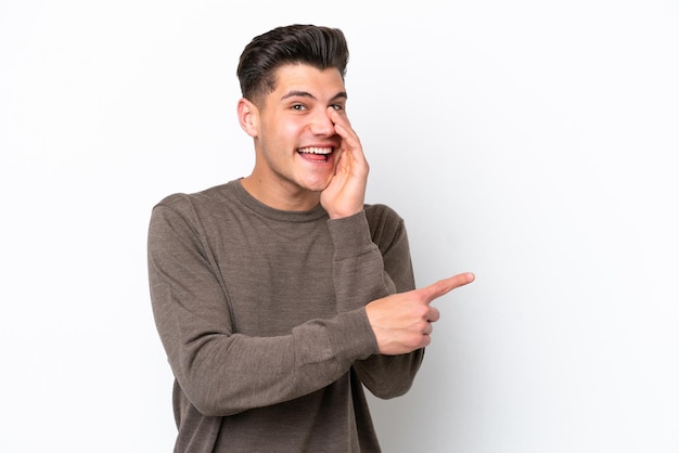 Young handsome caucasian man isolated on white bakcground pointing to the side to present a product and whispering something