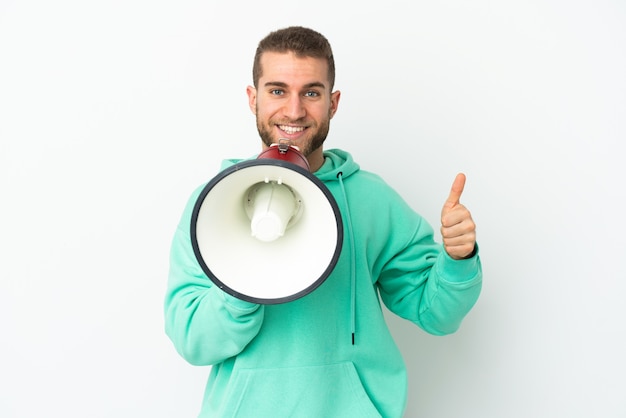 Young handsome caucasian man isolated on white wall holding a megaphone with thumb up