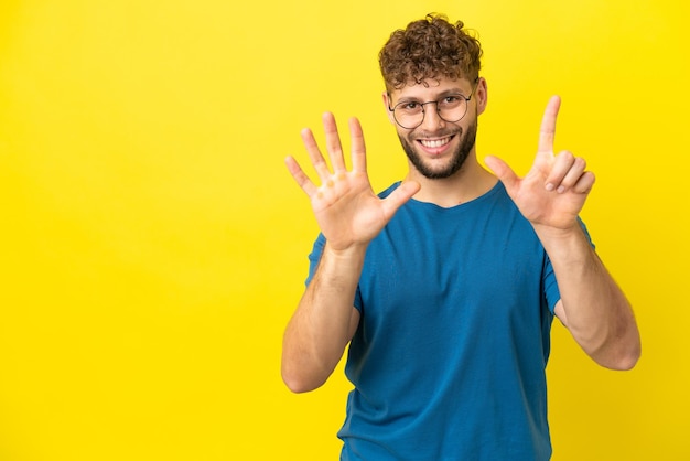 Giovane uomo caucasico bello isolato su sfondo giallo contando sette con le dita