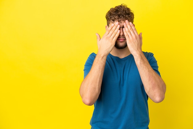 Young handsome caucasian man isolated on yellow background covering eyes by hands