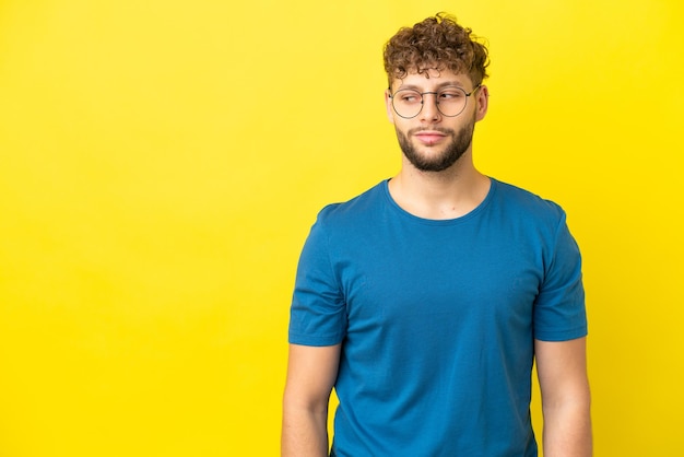 Young handsome caucasian man isolated on yellow background having doubts while looking side