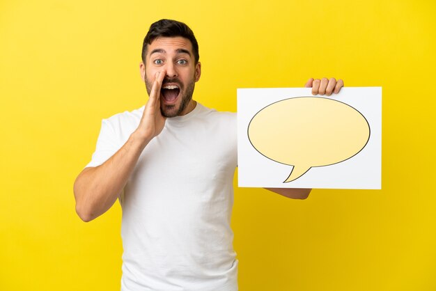 Young handsome caucasian man isolated on yellow background holding a placard with speech bubble icon and shouting