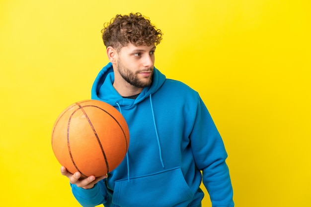 Молодой красивый кавказский мужчина изолирован на желтом фоне, играя в баскетбол