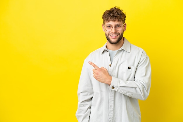 Giovane uomo caucasico bello isolato su sfondo giallo che indica il lato per presentare un prodotto
