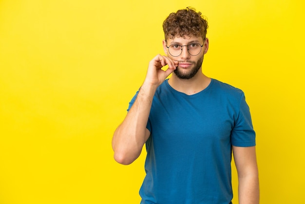 Young handsome caucasian man isolated on yellow background showing a sign of silence gesture