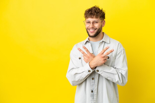 Young handsome caucasian man isolated on yellow background smiling and showing victory sign