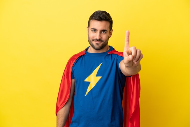 Young handsome caucasian man isolated on yellow background in superhero costume and pointing to the front