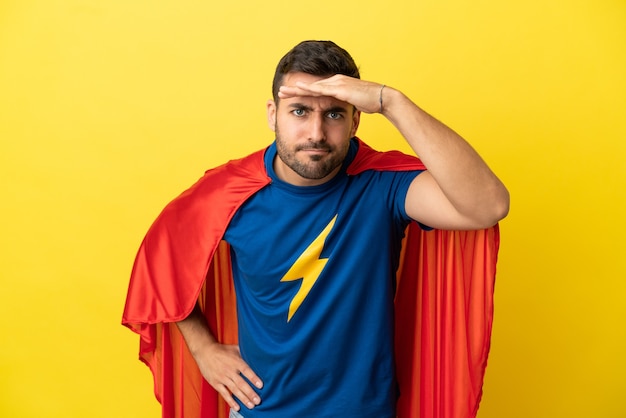 Photo young handsome caucasian man isolated on yellow background in superhero costume and showing something