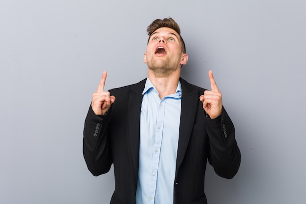 Young handsome caucasian man pointing upside with opened mouth.