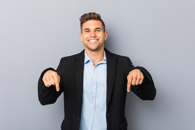 Young handsome caucasian man points down with fingers, positive feeling.