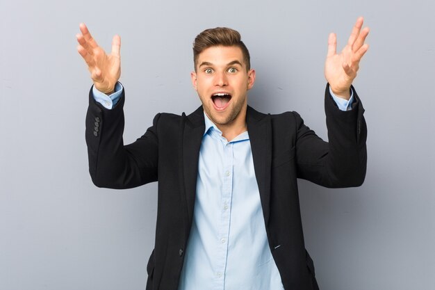 Young handsome caucasian man receiving a pleasant surprise, excited and raising hands.