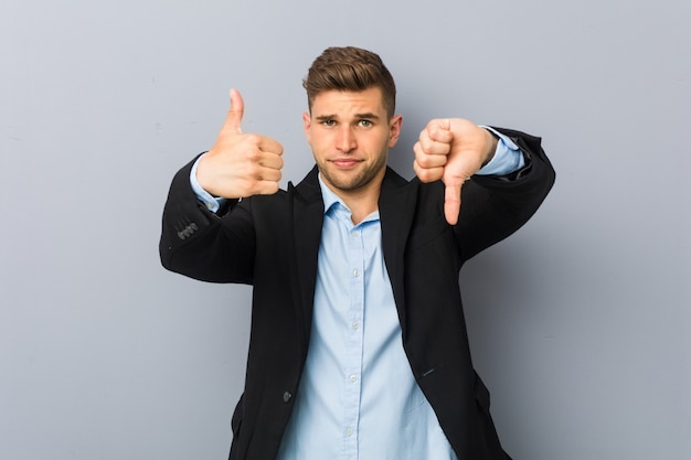 Young handsome caucasian man showing thumbs up and thumbs down, difficult choose concept