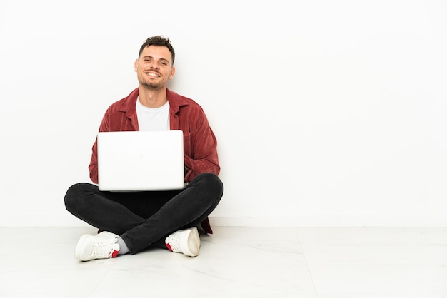 Young handsome caucasian man sit-in on the floor with laptop keeping the arms crossed in frontal position