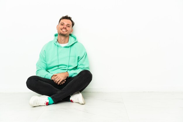 Young handsome caucasian man sitting on the floor laughing