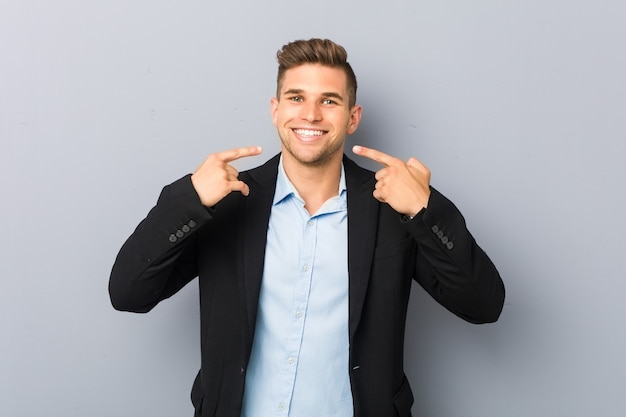 Young handsome caucasian man smiles, pointing fingers at mouth.