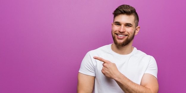 Giovane uomo caucasico bello che sorride e che indica da parte, mostrando qualcosa nello spazio.