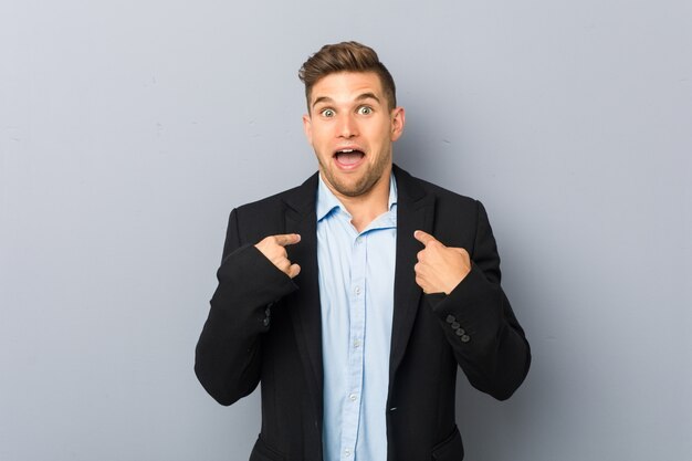 Young handsome caucasian man surprised pointing with finger, smiling broadly.