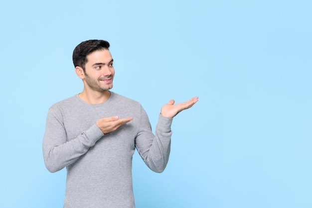 Young handsome Caucasian man with hands opening to copy space aside on isolated light blue background