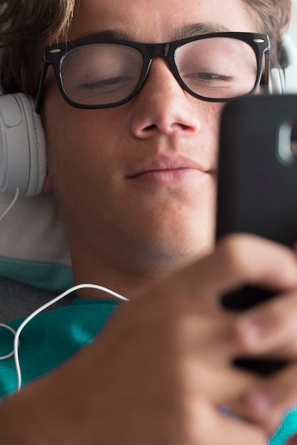 Young handsome caucasian teenager use cellular phone device and listen music with headphones lay down at home download songs activity and modern connected life concept