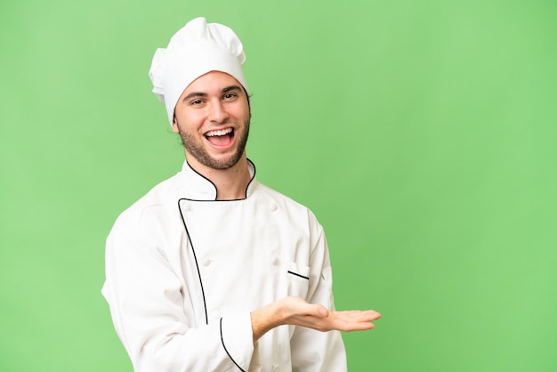 Молодой красивый шеф-повар на изолированном фоне представляет идею, улыбаясь