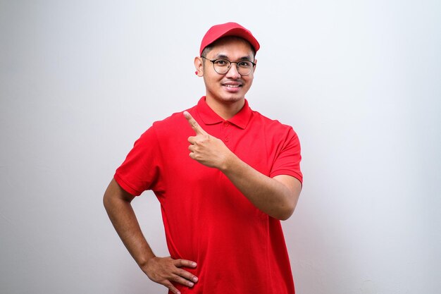 Young handsome chinese delivery man wearing cap standing over isolated white background with a big smile on face pointing with hand and finger to the side looking at the camera