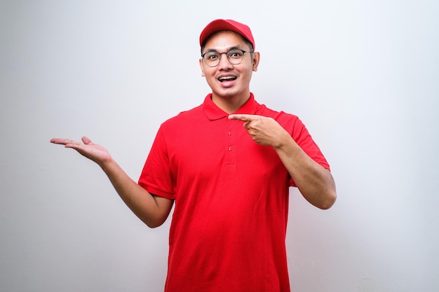 Young handsome chinese delivery man wearing cap standing over isolated white background with a big smile on face pointing with hand and finger to the side looking at the camera