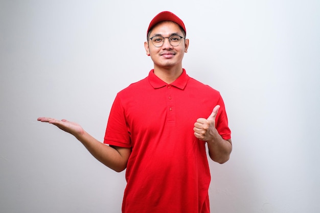 Young handsome chinese delivery man wearing cap standing over isolated white background with a big smile on face pointing with hand and finger to the side looking at the camera