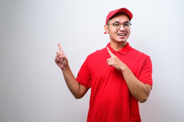 Young handsome chinese delivery man wearing cap standing over isolated white background with a big smile on face pointing with hand and finger to the side looking at the camera