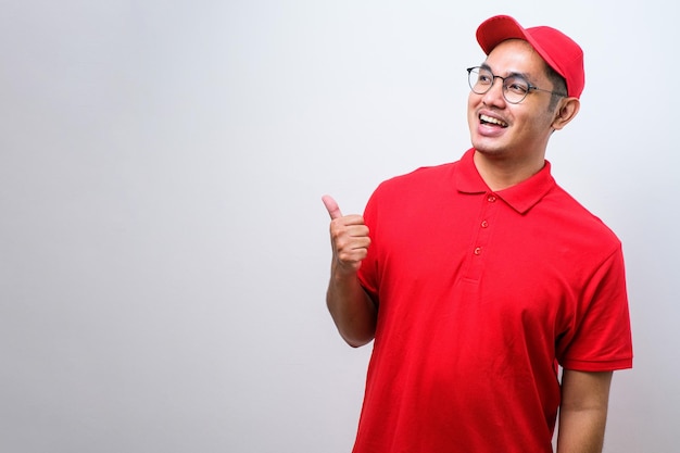 Young handsome chinese delivery man wearing cap standing over isolated white background with a big smile on face pointing with hand and finger to the side looking at the camera