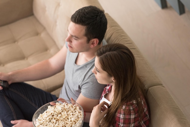 彼らの豪華な家の別荘でポップコーンとテレビを見て自由な時間を楽しんでいる若いハンサムなカップル