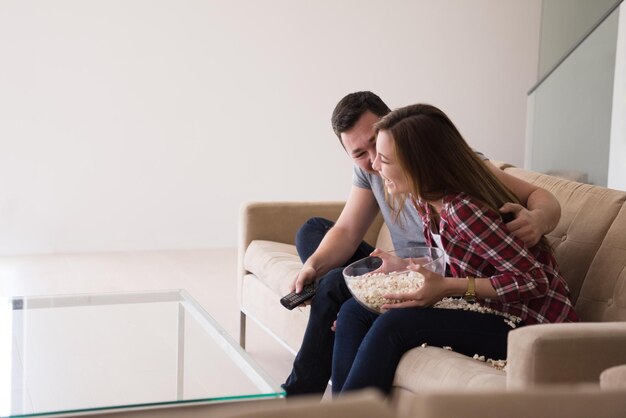 Young handsome couple enjoying free time watching television\
with popcorn in their luxury home villa