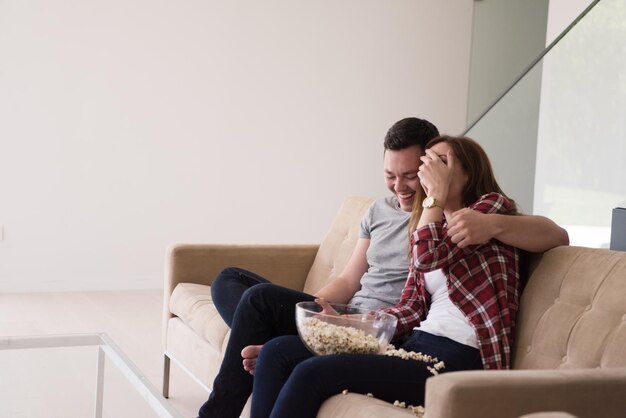 молодая красивая пара наслаждается свободным временем, смотря телевизор с попкорном на своей роскошной домашней вилле