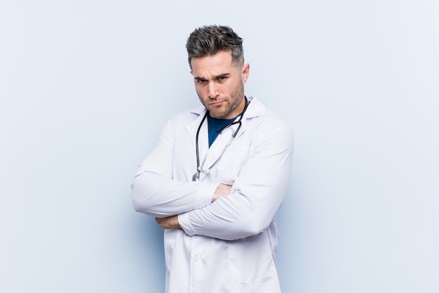 Young handsome doctor man frowning face in displeasure, keeps arms folded.